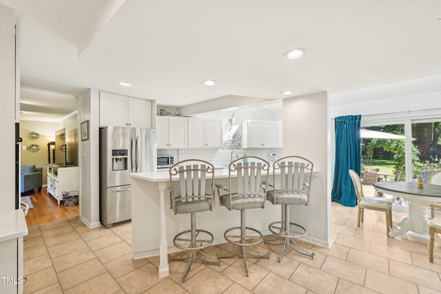 kitchen featuring appliances with stainless steel finishes, light countertops, white cabinets, a kitchen bar, and backsplash