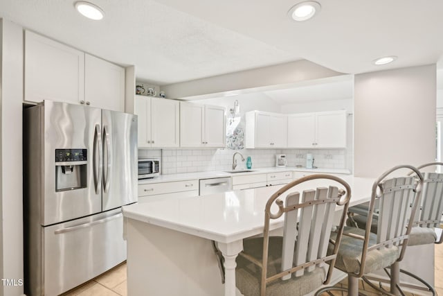 kitchen featuring appliances with stainless steel finishes, a sink, a breakfast bar, light countertops, and tasteful backsplash