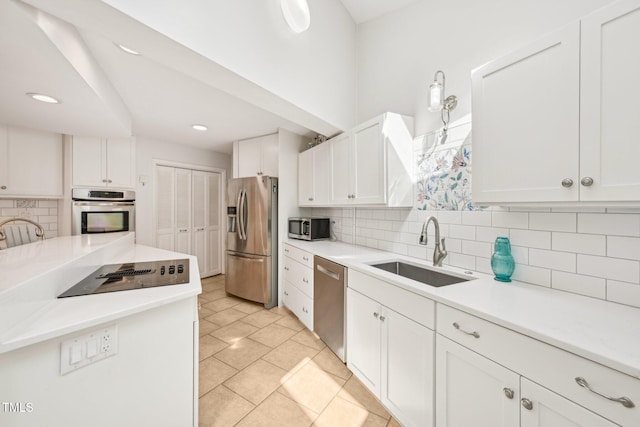 kitchen with appliances with stainless steel finishes, a sink, tasteful backsplash, white cabinets, and light countertops