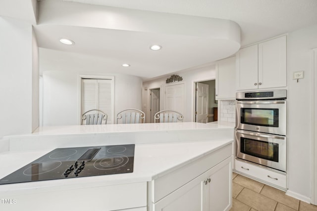kitchen with black electric stovetop, double oven, white cabinetry, light tile patterned flooring, and recessed lighting