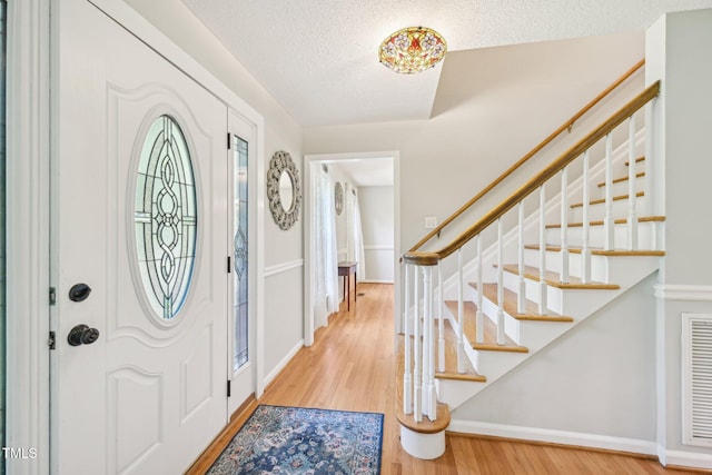 foyer entrance with wood finished floors, a textured ceiling, baseboards, and stairway