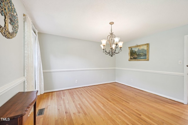 empty room featuring light wood-type flooring, a chandelier, and baseboards