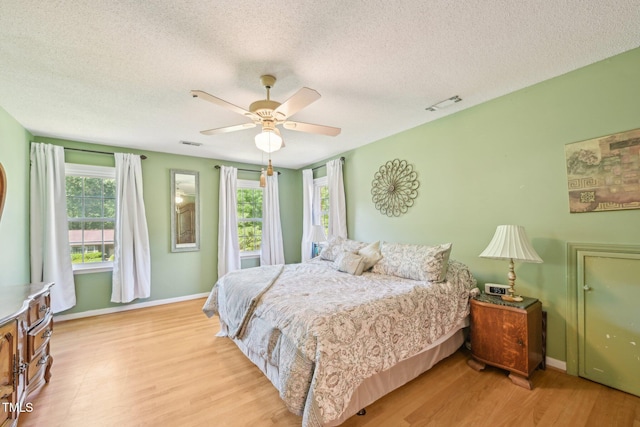 bedroom featuring a textured ceiling, light wood finished floors, baseboards, and ceiling fan
