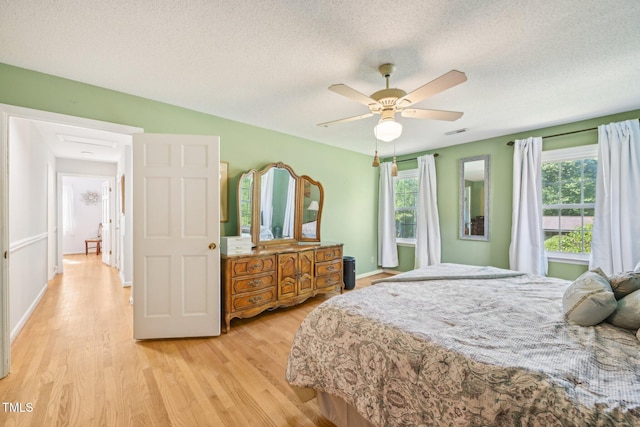 bedroom with light wood-style flooring, a textured ceiling, ceiling fan, and baseboards
