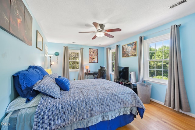 bedroom with multiple windows, light wood-style floors, ceiling fan, baseboards, and a textured ceiling