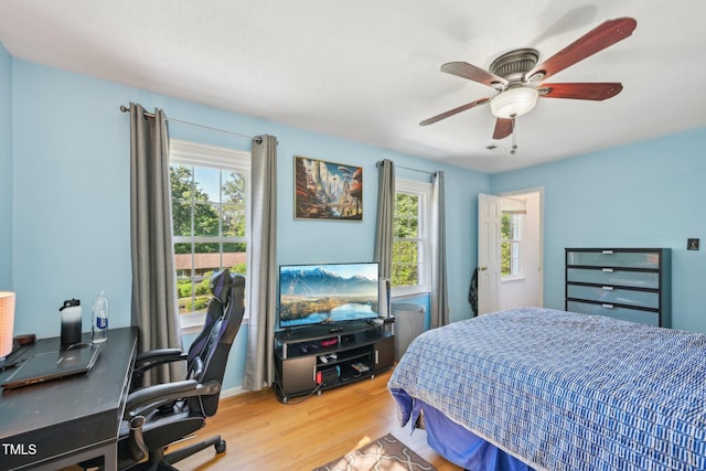 bedroom featuring multiple windows, wood finished floors, an office area, and ceiling fan