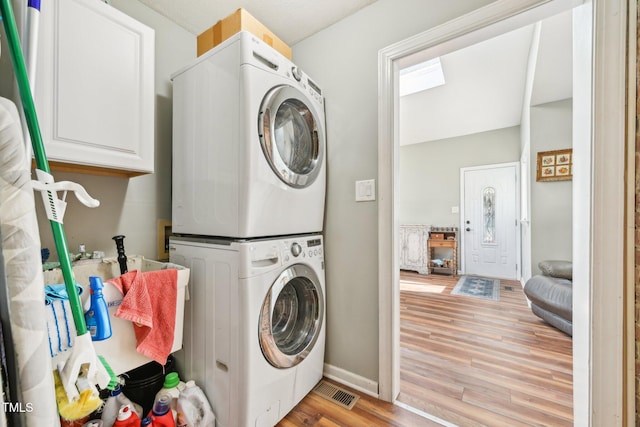 washroom featuring stacked washer / dryer, light wood finished floors, cabinet space, and baseboards