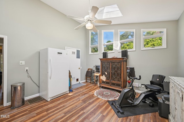 interior space with a skylight, wood finished floors, a ceiling fan, a desk, and baseboards