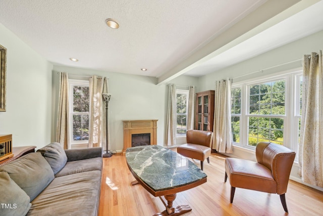 living room with a textured ceiling, a glass covered fireplace, light wood-style floors, and recessed lighting