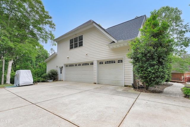 view of property exterior with driveway, a shingled roof, and a garage