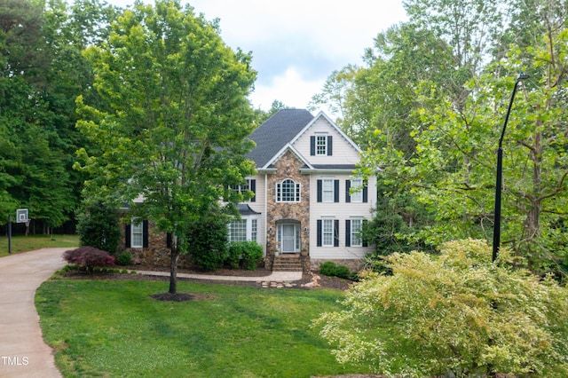 view of front of home featuring stone siding, a front yard, and concrete driveway