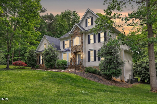 view of front of home featuring stone siding, a lawn, and central air condition unit