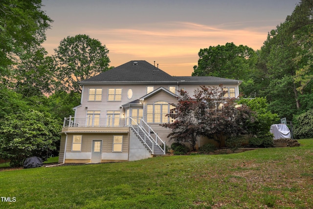 back of property at dusk featuring stairs, a lawn, and a wooden deck