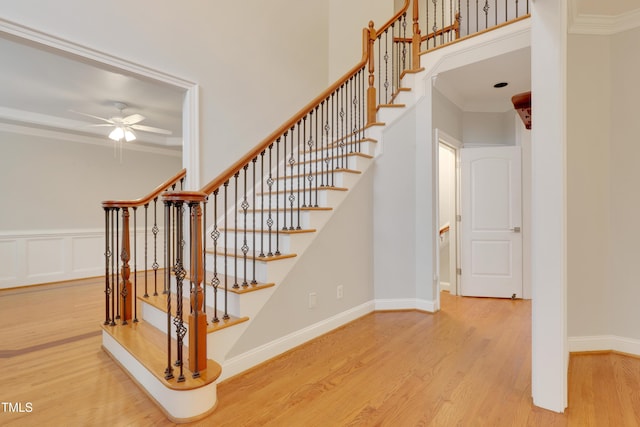 stairs featuring wood finished floors, a ceiling fan, crown molding, and a high ceiling