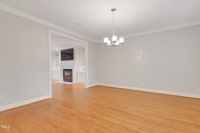 spare room with crown molding, light wood-style floors, a chandelier, baseboards, and built in features