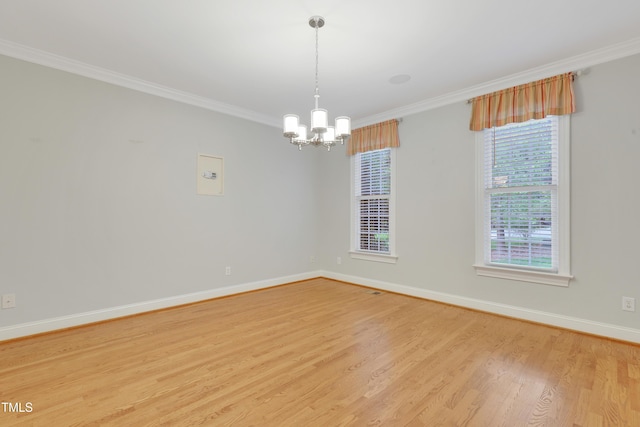 spare room featuring a chandelier, light wood-style floors, crown molding, and baseboards