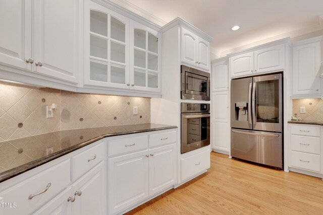 kitchen with stainless steel appliances, glass insert cabinets, dark stone countertops, white cabinets, and light wood finished floors