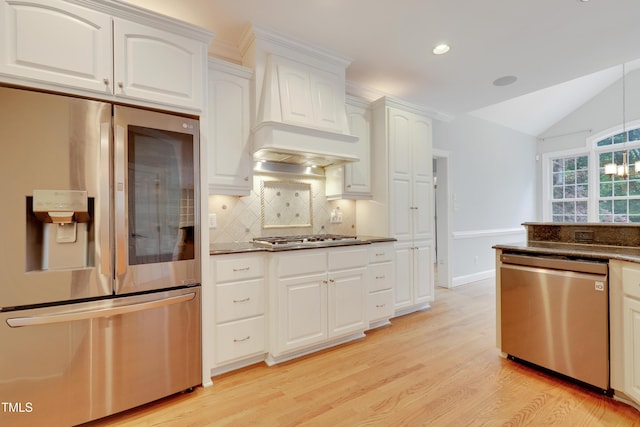 kitchen with appliances with stainless steel finishes, light wood-style flooring, vaulted ceiling, backsplash, and white cabinetry