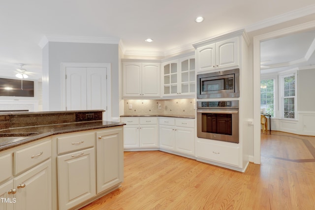 kitchen with stainless steel appliances, light wood-style floors, dark stone counters, white cabinetry, and crown molding