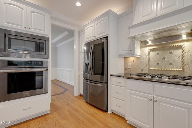 kitchen with stainless steel appliances, exhaust hood, ornamental molding, white cabinets, and light wood-type flooring