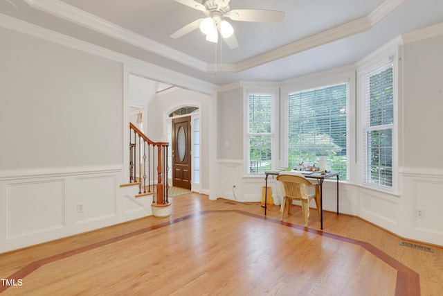 entryway featuring light wood-type flooring, healthy amount of natural light, a decorative wall, a ceiling fan, and crown molding