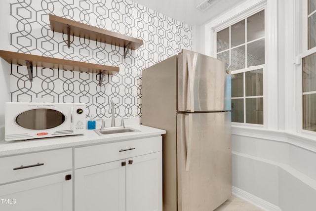 kitchen with freestanding refrigerator, open shelves, a sink, light countertops, and white cabinetry