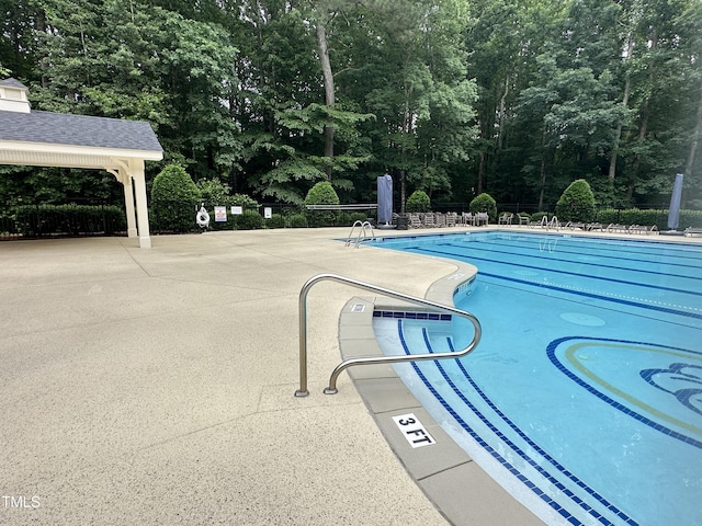 community pool with fence, a patio, and view of scattered trees