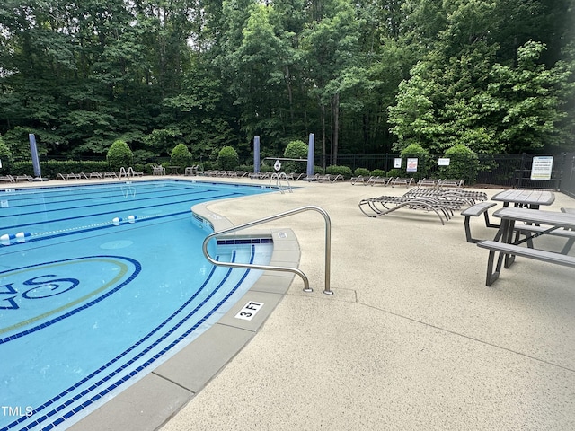 community pool featuring fence, a patio, and a wooded view