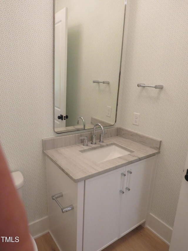 bathroom with wood finished floors, baseboards, vanity, and toilet