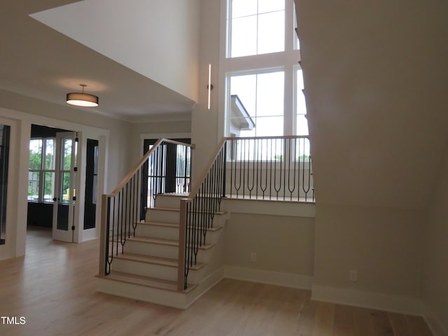 staircase with wood finished floors, baseboards, and a towering ceiling