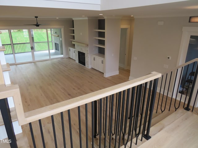 unfurnished living room with light wood-style flooring, ceiling fan, ornamental molding, built in shelves, and a glass covered fireplace