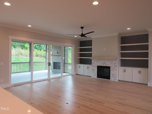 unfurnished living room with a glass covered fireplace, light wood-style floors, ornamental molding, recessed lighting, and built in features