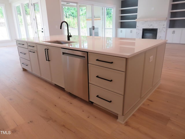 kitchen featuring dishwasher, a sink, light wood-style flooring, light countertops, and a glass covered fireplace