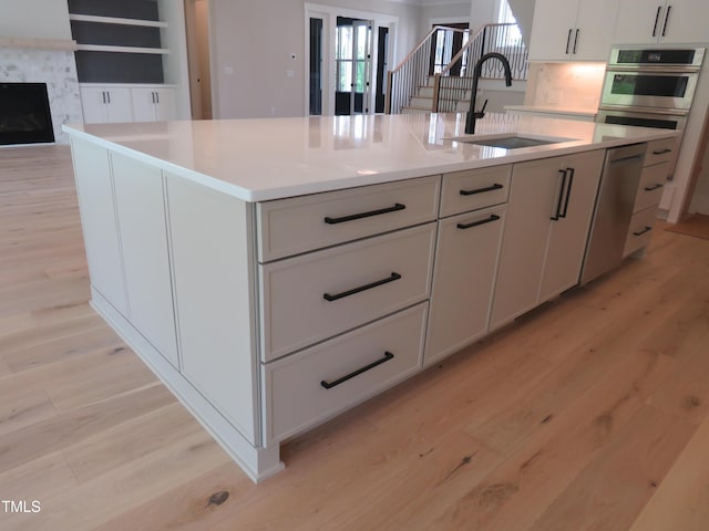 kitchen with a sink, light wood-style flooring, a kitchen island with sink, and stainless steel appliances