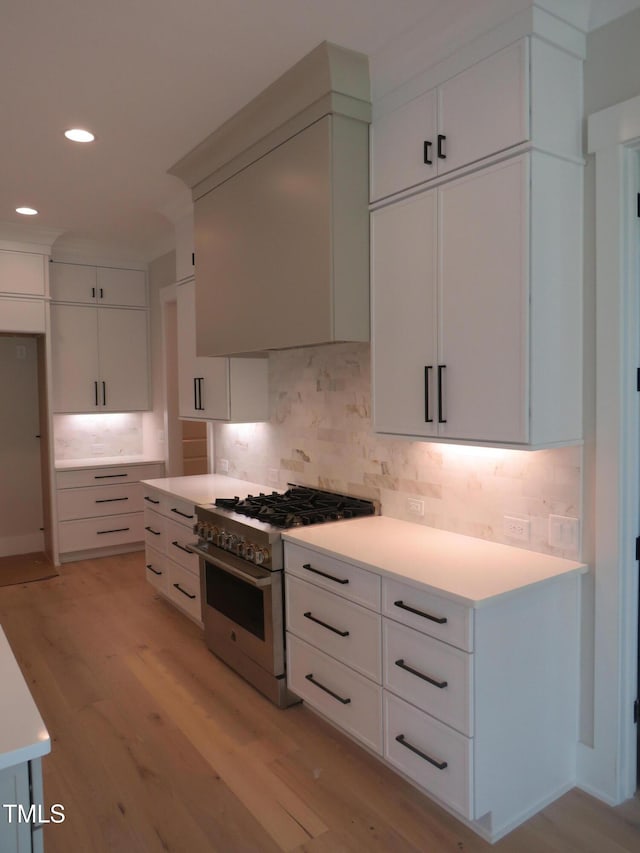 kitchen featuring high end stainless steel range oven, light wood-style floors, decorative backsplash, recessed lighting, and light countertops