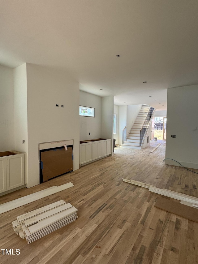 unfurnished living room with stairway, light wood-type flooring, and a healthy amount of sunlight
