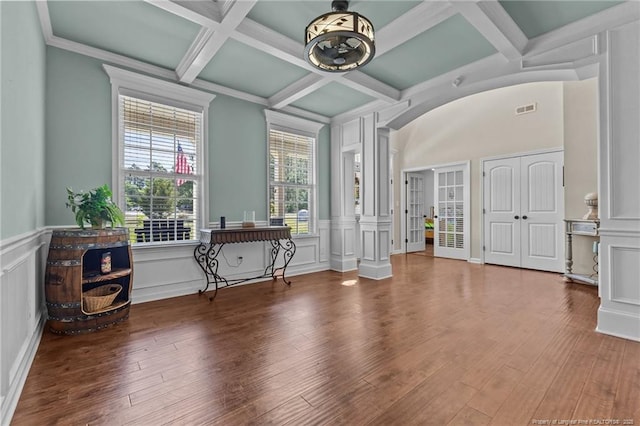 spare room with coffered ceiling, a decorative wall, beamed ceiling, wood finished floors, and a wainscoted wall