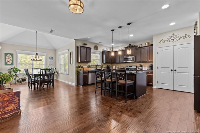 kitchen with stainless steel appliances, dark brown cabinets, a kitchen breakfast bar, a center island, and a chandelier