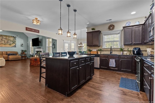 kitchen with appliances with stainless steel finishes, dark countertops, a breakfast bar, open floor plan, and dark wood finished floors