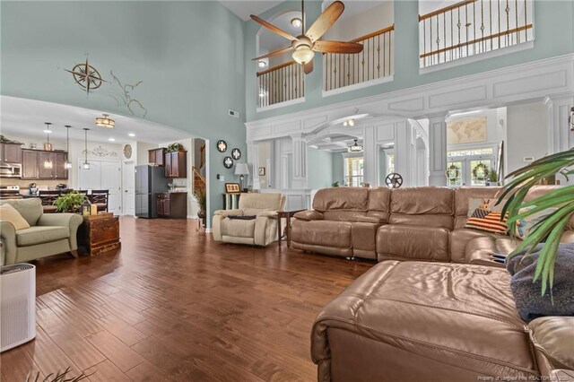 living area with a ceiling fan, a towering ceiling, dark wood-type flooring, and ornate columns