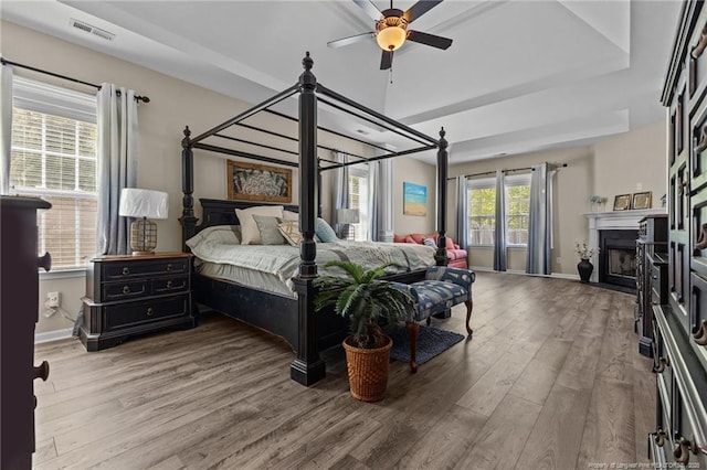 bedroom featuring wood finished floors, baseboards, a fireplace with flush hearth, and a ceiling fan