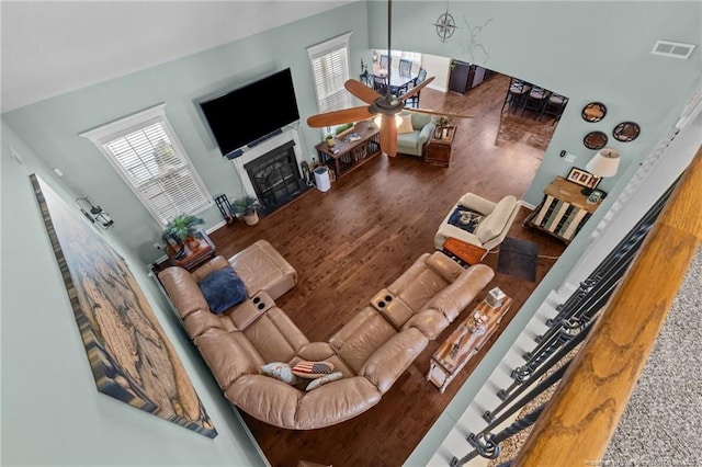 living room featuring wood finished floors, a fireplace with flush hearth, ceiling fan, and a towering ceiling
