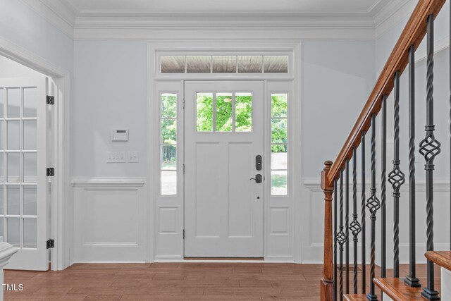 entrance foyer featuring crown molding, wainscoting, a decorative wall, stairs, and light wood-style flooring