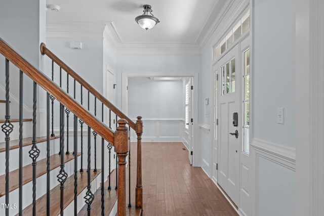 foyer featuring hardwood / wood-style floors, a decorative wall, stairs, wainscoting, and crown molding