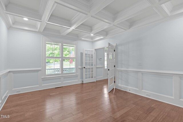 empty room featuring beam ceiling, wood finished floors, coffered ceiling, french doors, and a decorative wall