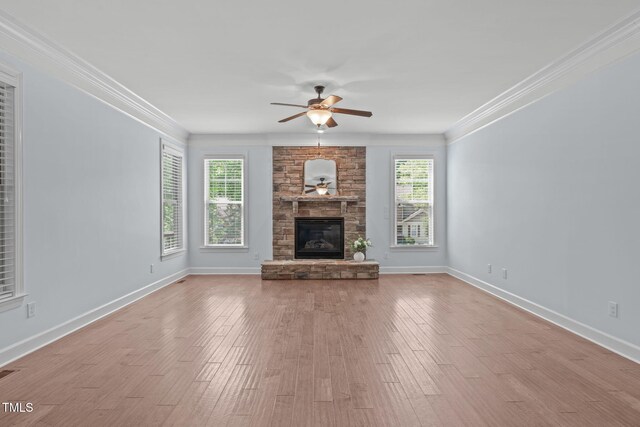 unfurnished living room featuring a ceiling fan, a stone fireplace, wood finished floors, crown molding, and baseboards