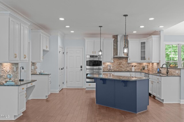 kitchen featuring wall chimney range hood, stainless steel double oven, a sink, white cabinets, and recessed lighting
