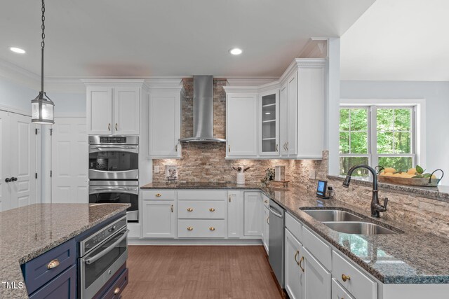 kitchen featuring stainless steel appliances, a sink, wall chimney range hood, white cabinetry, and decorative backsplash