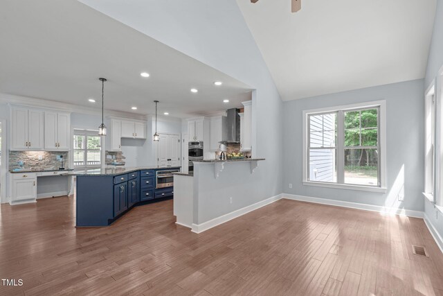 kitchen featuring blue cabinetry, wall chimney exhaust hood, white cabinets, tasteful backsplash, and recessed lighting