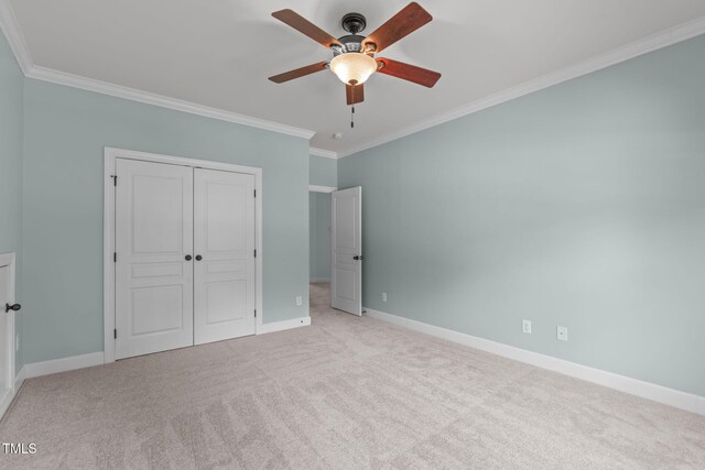 unfurnished bedroom featuring ornamental molding, baseboards, a closet, carpet floors, and a ceiling fan
